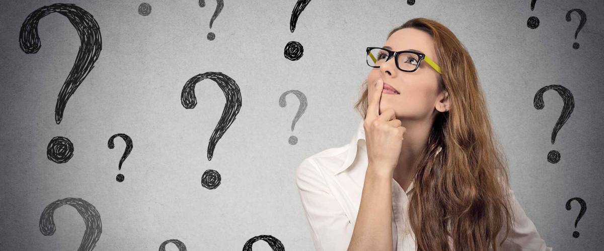 Thinking business woman with glasses looking up on many questions mark isolated on gray wall background