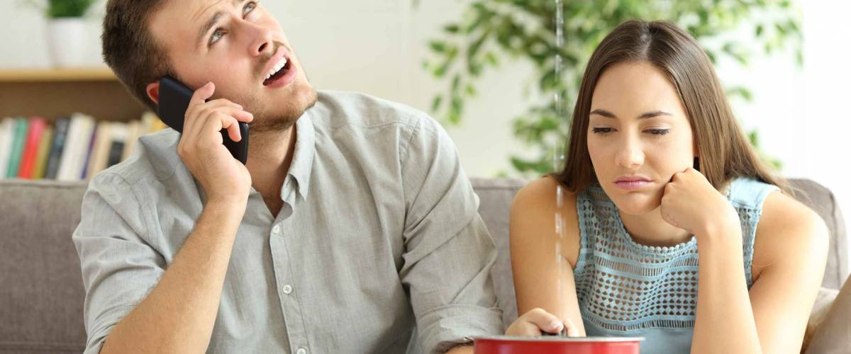 Upset couple sitting in a couch in the living room and calling insurance for home leaks