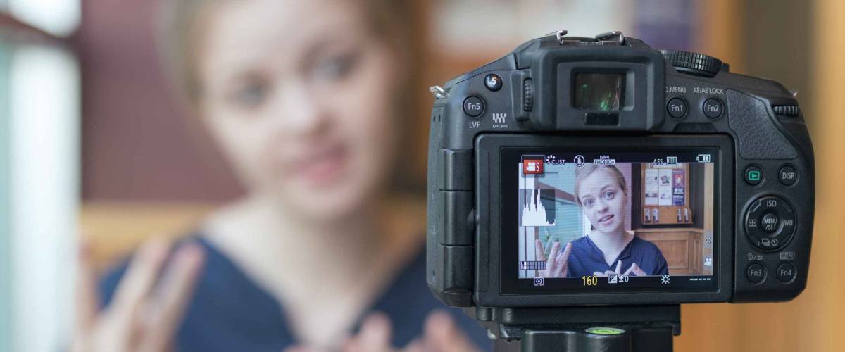 Makati, Philippines - April 8, 2018: Camera recording a young caucasian female blogger gesturing while making a video, selective focus on camera