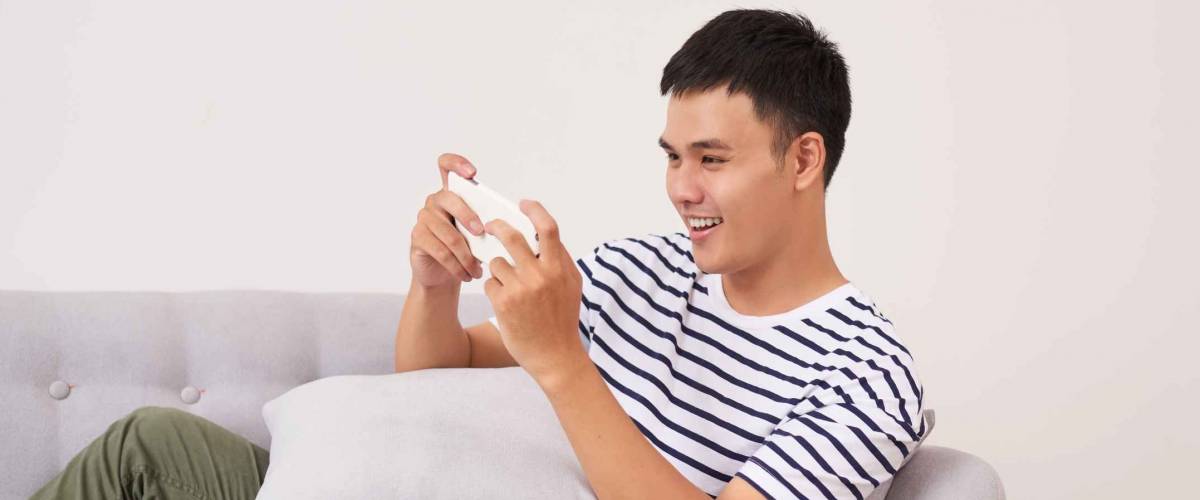 Young asian man sitting on sofa and playing games on phone at home