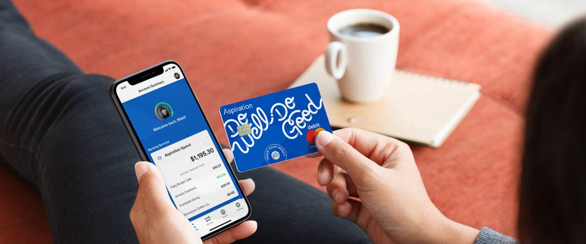 Young person holding phone displaying Aspiration app and holding Aspiration debit card