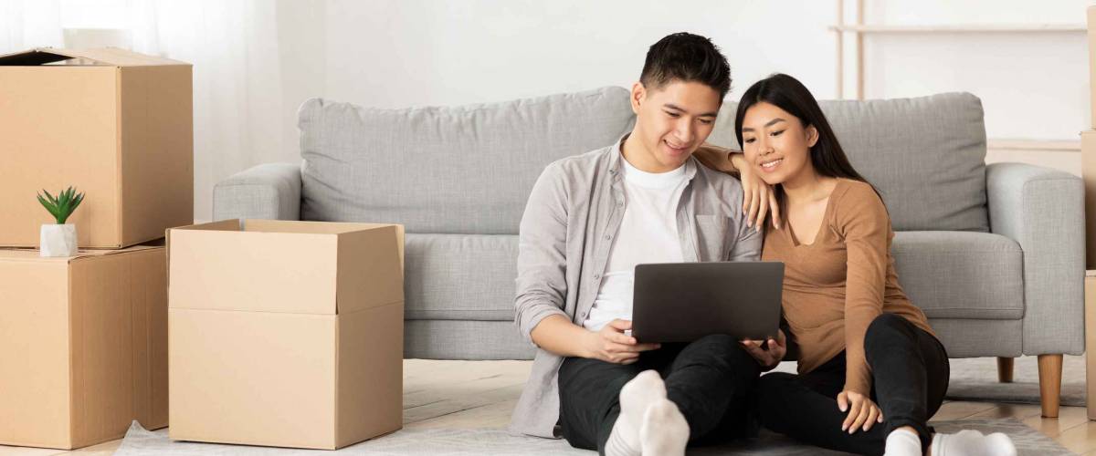 Asian family using laptop sitting on floor among boxes, empty space