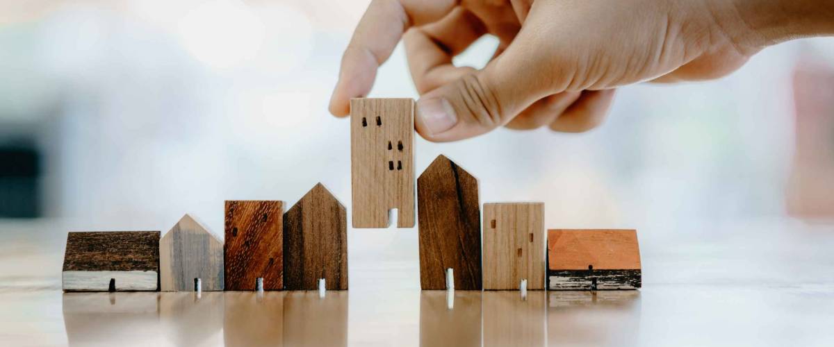 Hand choosing mini wood house models, representing different mortgage types
