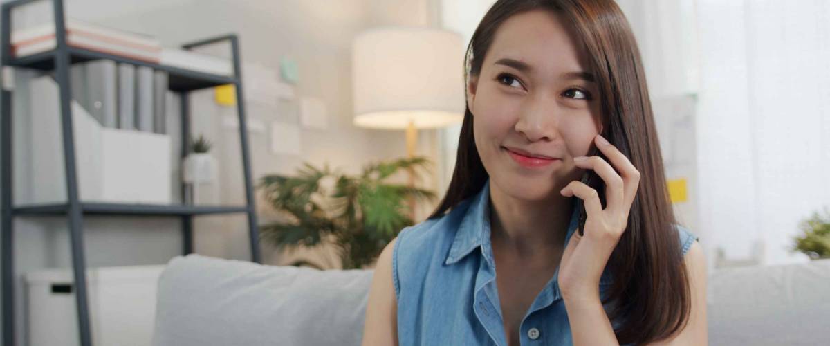 Young Asian-American woman sitting on sofa and talking on mobile phone