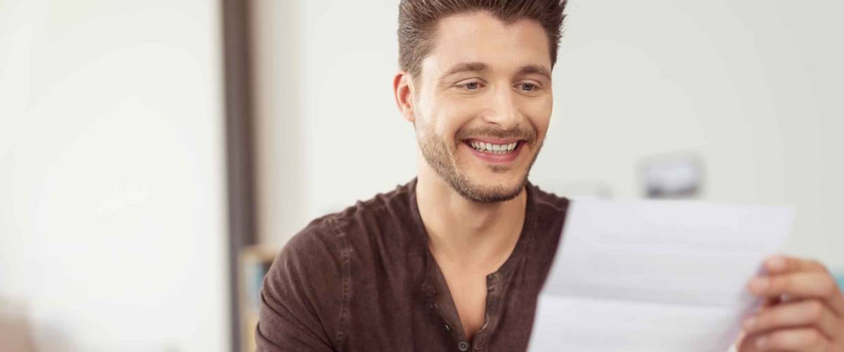 Close up Good Looking Young Bearded Guy Reading a Letter at the Couch with a Happy Facial Expression