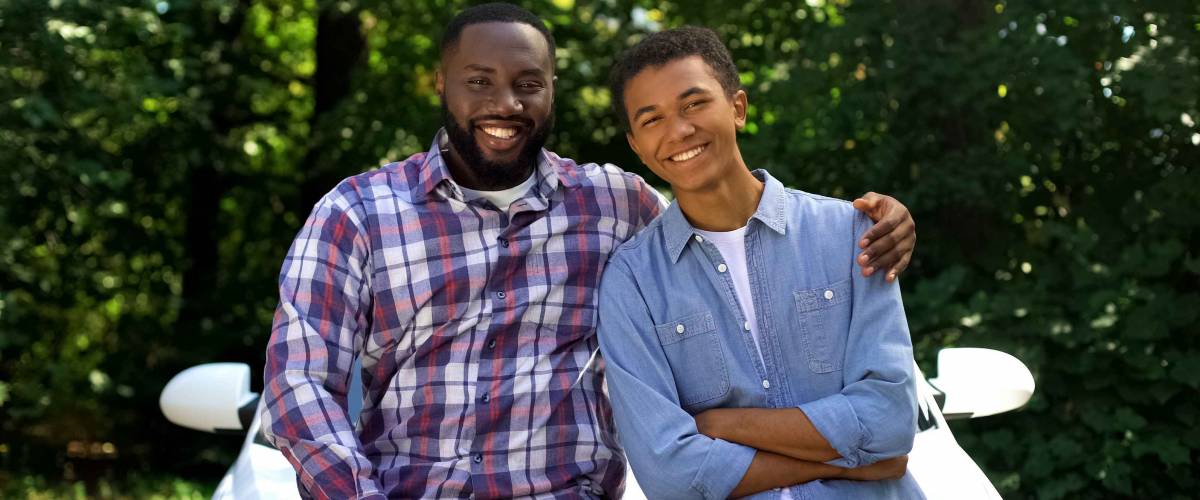 Father hugging teenage male child smiling on camera standing auto background