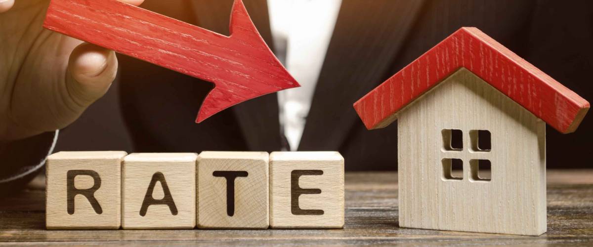 Businessman holding the down arrow on wooden blocks with the word Rate and house. Low interest in mortgages. Reducing interest payments for mortgage. The fall in housing rates on credit.