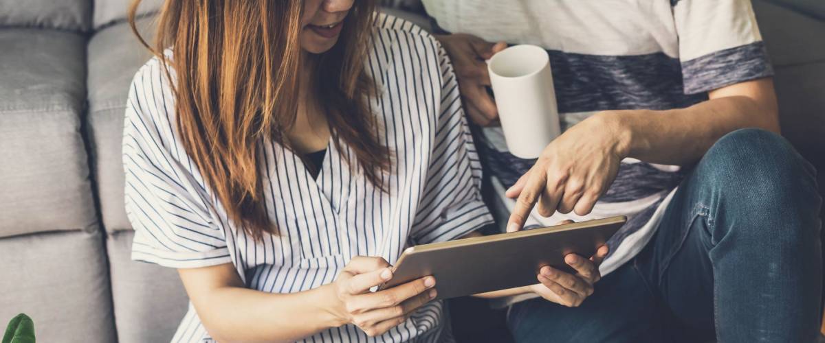 Young happy couple moving in new home, sitting and relaxing on the floor and shopping online with tablet