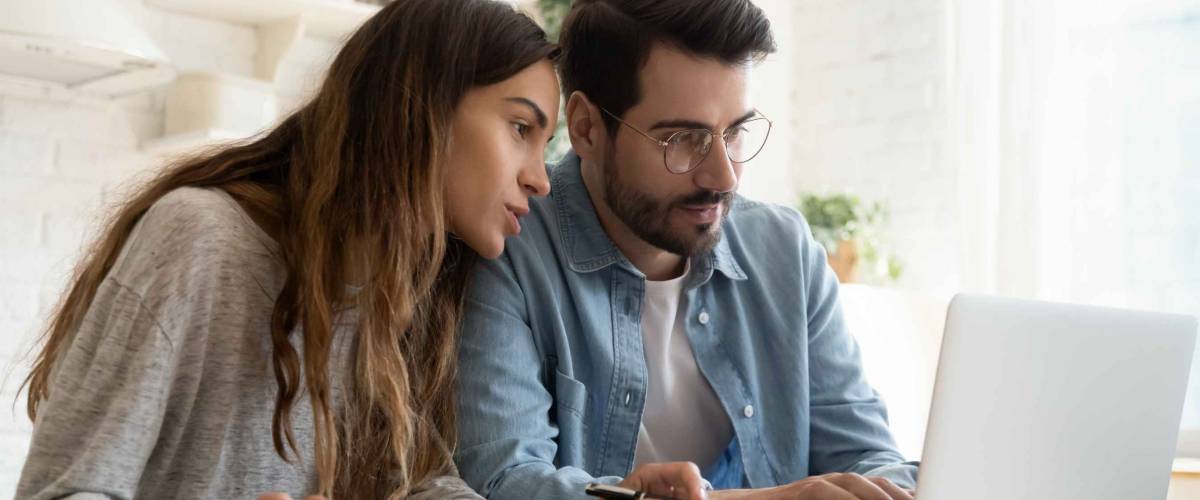 Focused young couple calculating bills, discussing planning budget together, serious wife and husband looking at laptop screen, using online banking services and calculator, checking finances