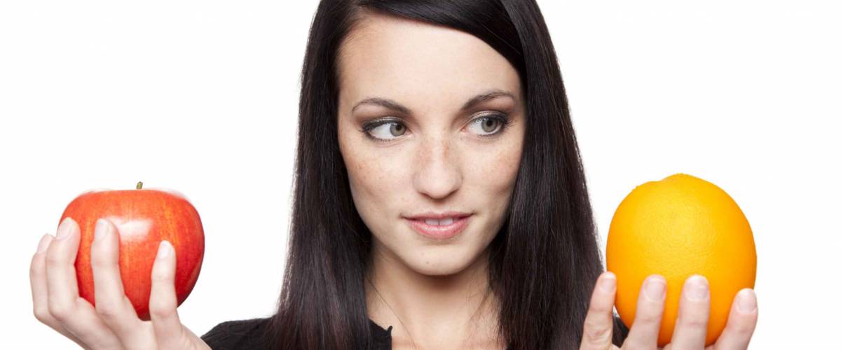 Isolated studio shot of a dark haired caucasian woman comparing apples to oranges.
