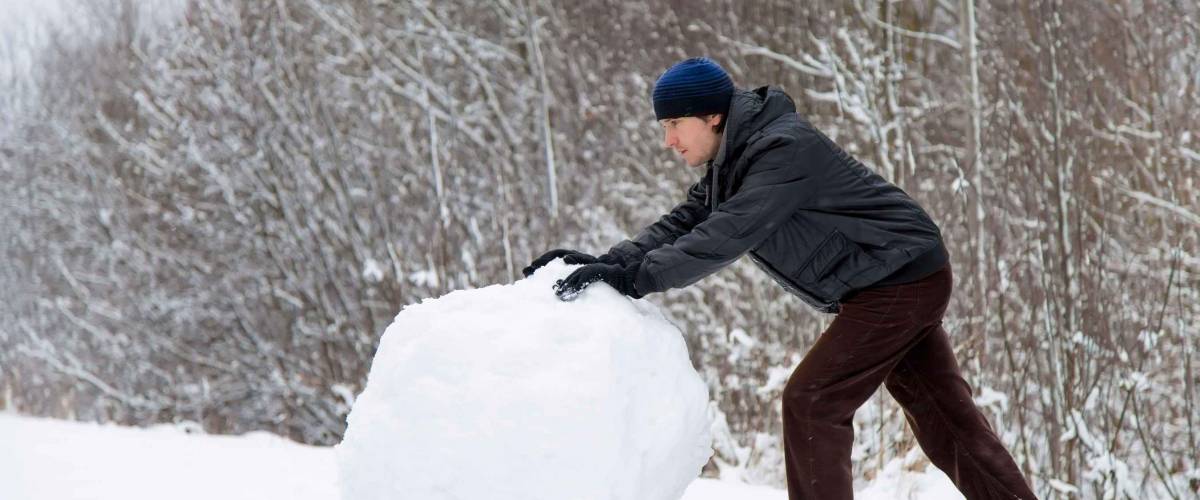 Boy rolls a big snowball to build a snowman in winter day