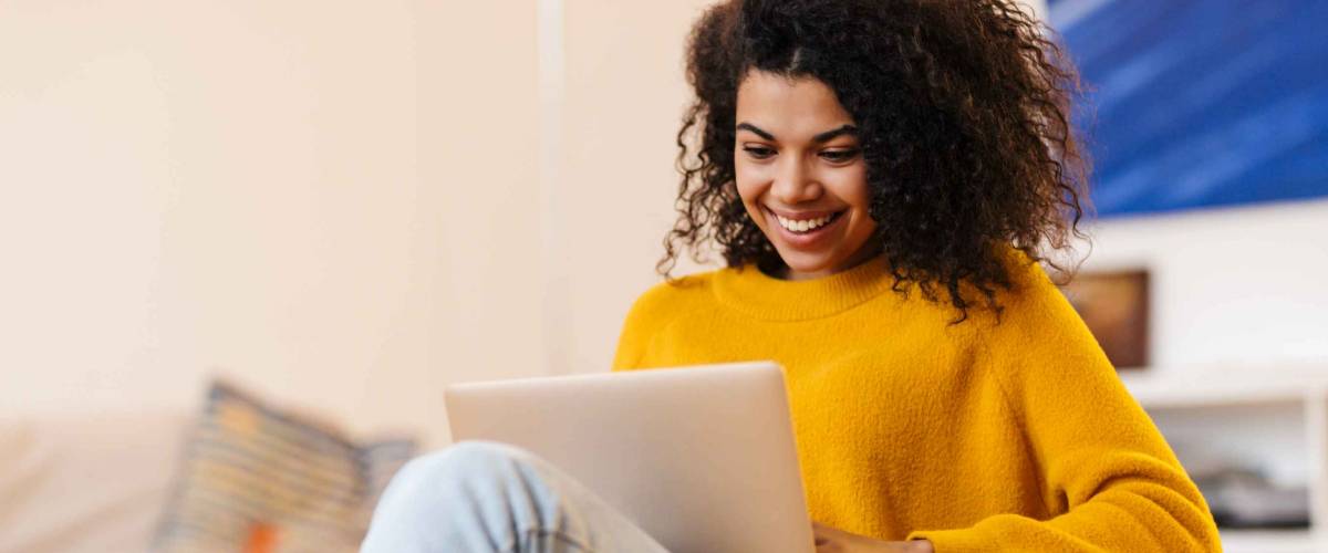 Image of cheerful african american woman using laptop while sitting on chair in living room