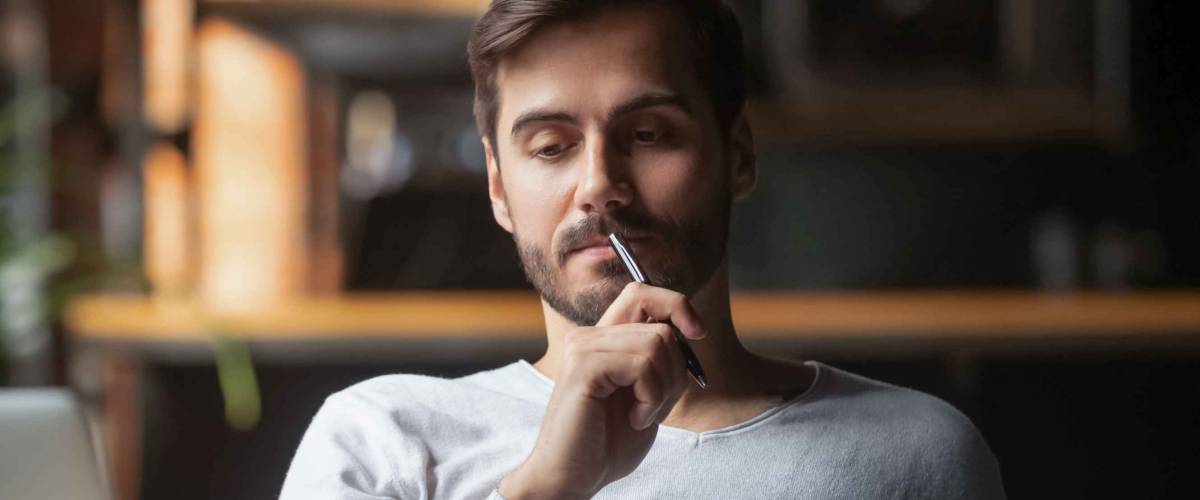 Pensive bearded man sitting at table drink coffee work at laptop thinking of problem solution, thoughtful male employee pondering considering idea looking at computer screen making decision