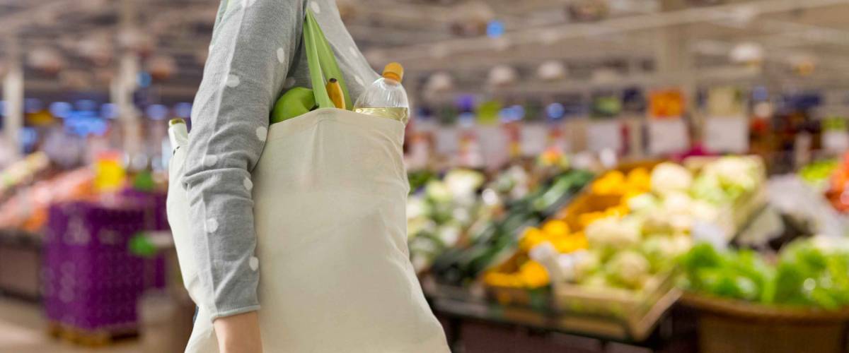 consumerism, eating and eco friendly concept - woman with white reusable canvas bag for food shopping over supermarket on background