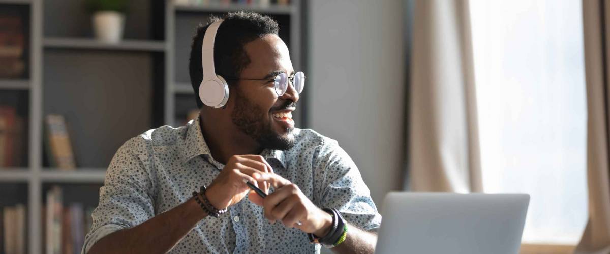 Happy relaxed millennial afro american business man wear wireless headphones look away rest at workplace