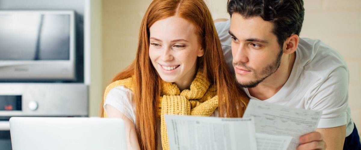 Couple holding financial statements looking at computer