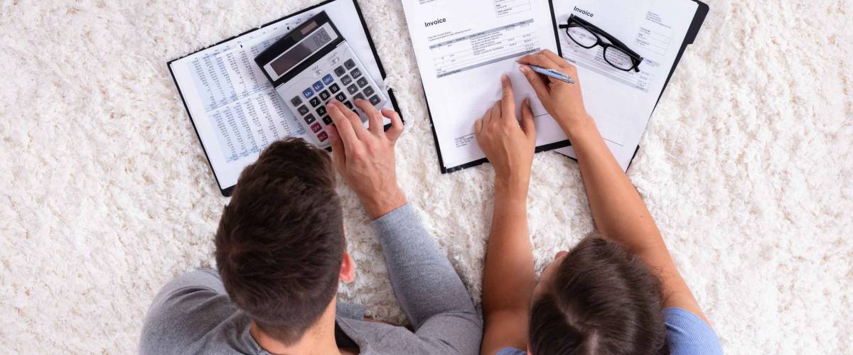Overhead View Of Young Couple Calculating Invoice On Fluffy Carpet