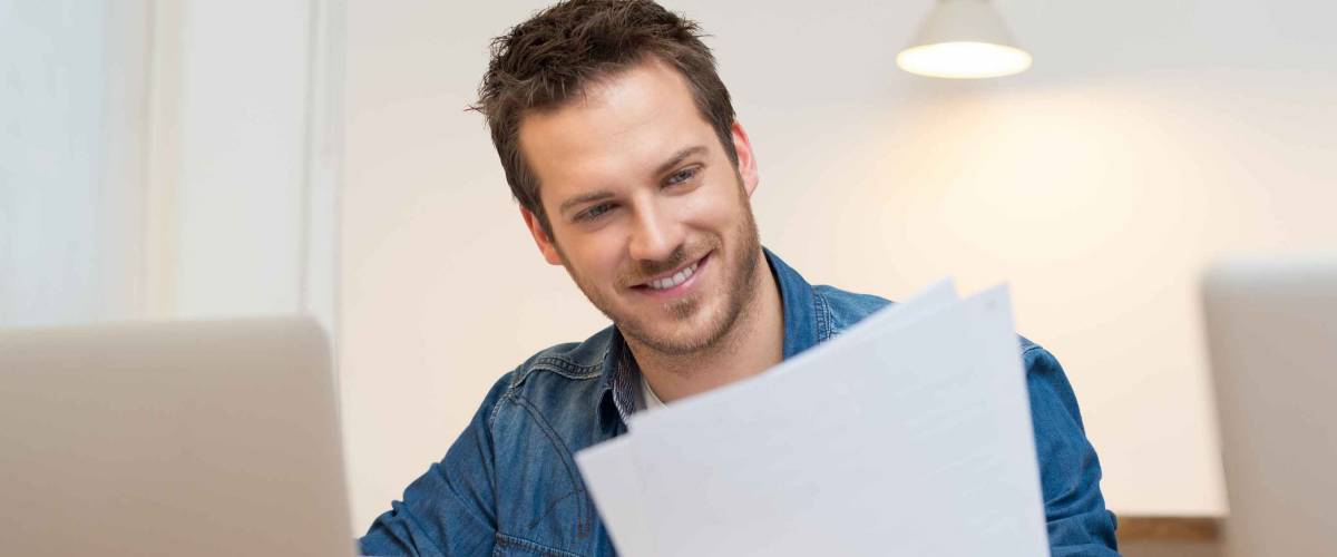 Happy young businessman reading paperwork at desk in office