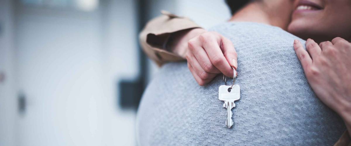 Young woman holding keys hugging husband in front of their new home after buying real estate