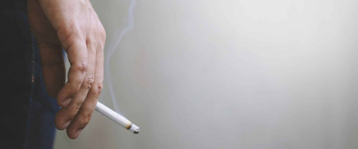 man holding smoking a cigarette in hand. Cigarette smoke spread. dark background