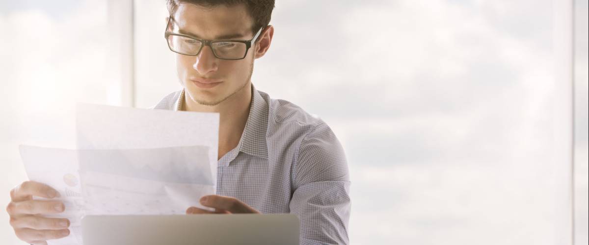 Young caucasian businessman in glasses looking carefully and business report