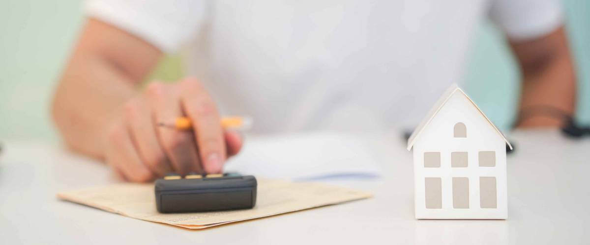 close up young house's model with man hand pressing calculator for check and summary expense of home loan mortgage for refinance plan , people lifestyle and work from home concept
