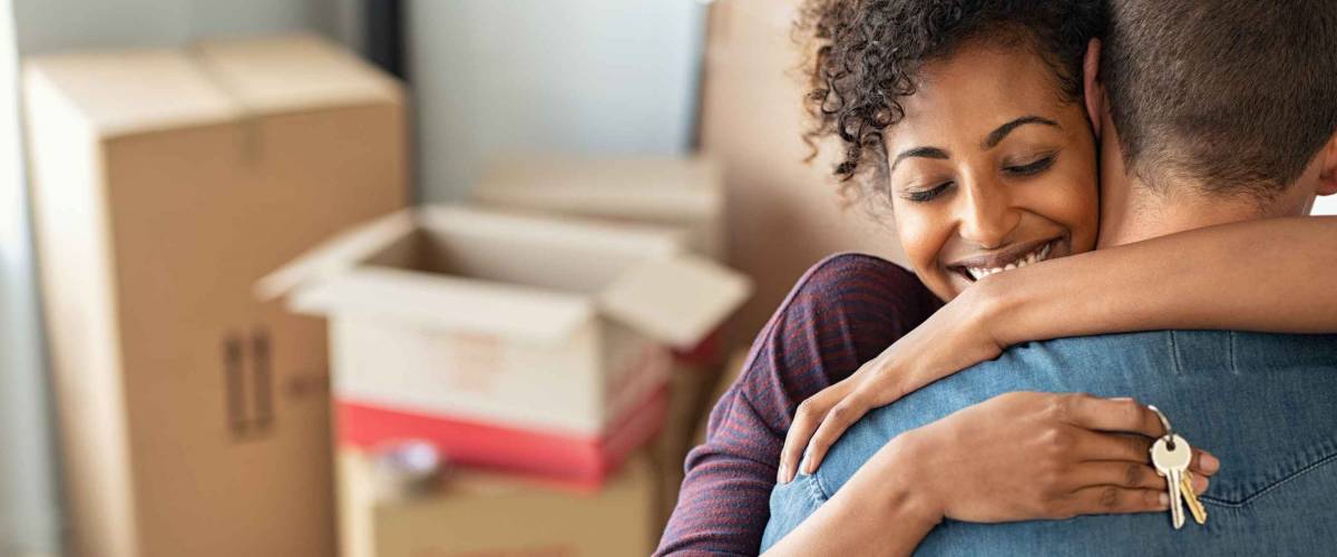 Young african woman holding home keys while hugging boyfriend