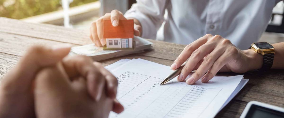 Loan agreement, real estate agent or bank officer describes the loan interest to the customer, along with loan documents with a home-style pen and a replica money on a wooden table.