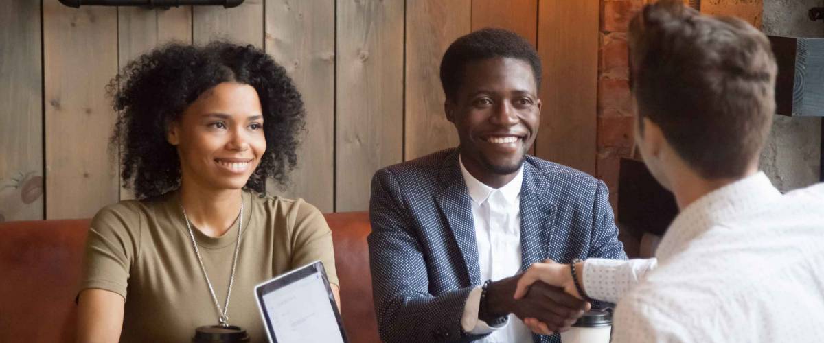 Smiling african american couple shaking hands to mortgage insurance broker with wood paneling behind them