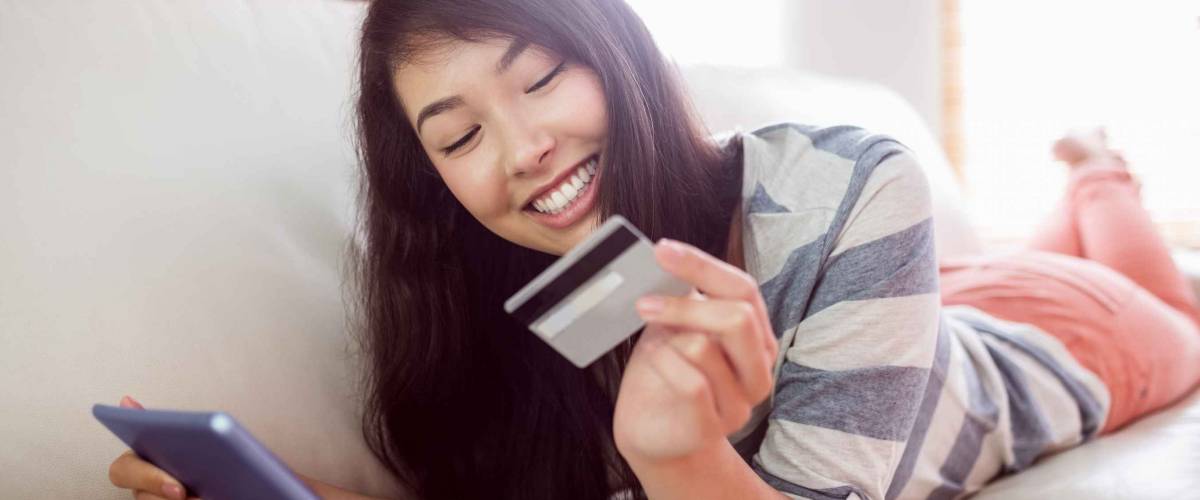 Smiling asian woman on couch using tablet to shop online at home in the living room