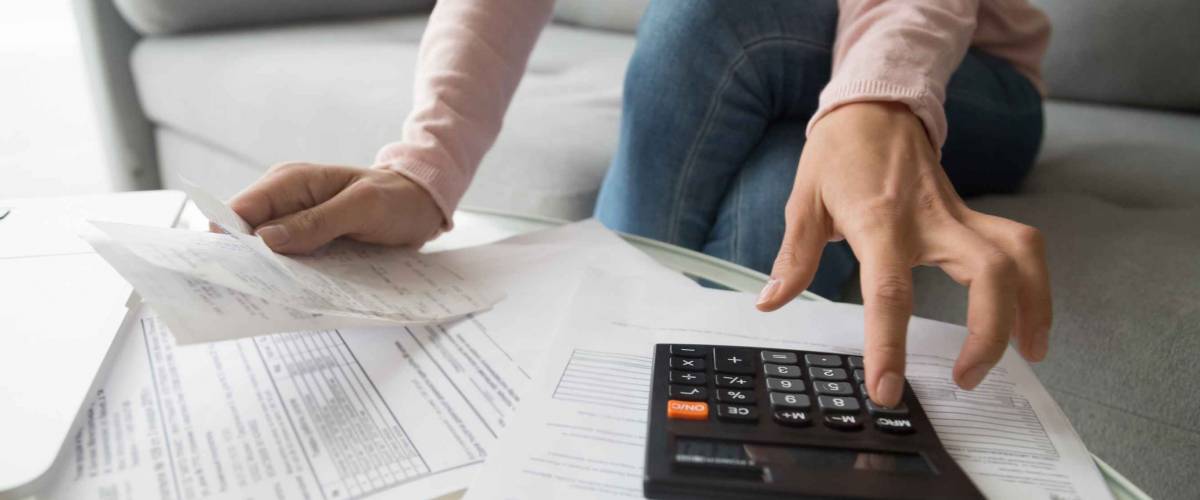 woman in pink shirt sits on a couch and looks at papers while punching numbers into calculator