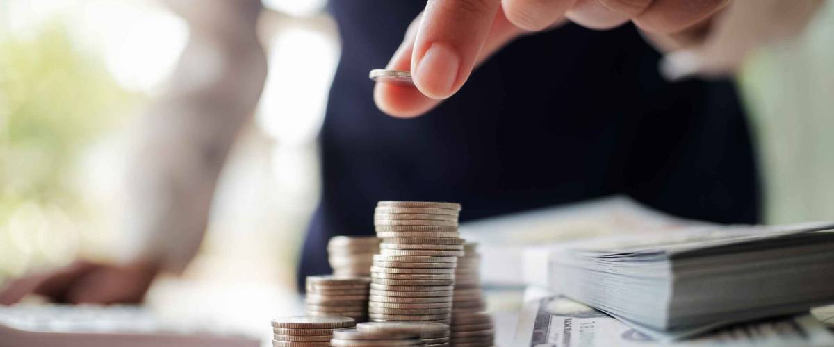 hand placing a coin on a stack, with cash bundled beside it