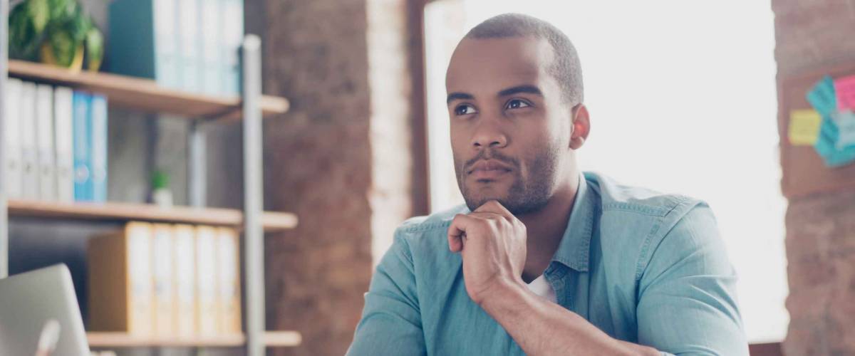 man sitting at desk with hand on chin, looking contemplative