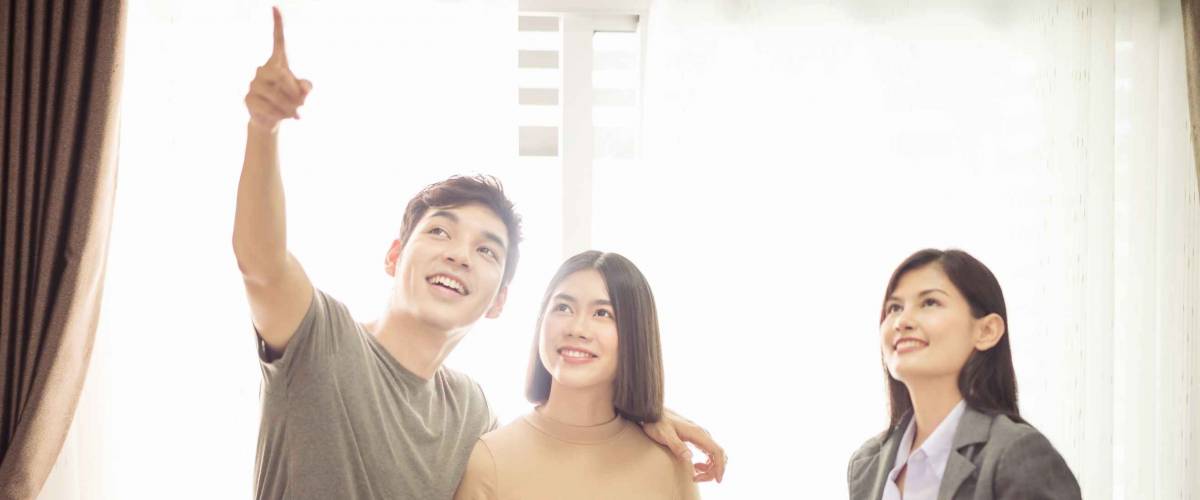 young couple smiling with real estate agent in front of light-filled window