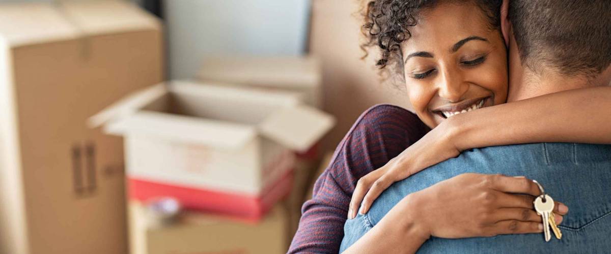 Young woman holding home keys while hugging man with cardboard boxes in the background