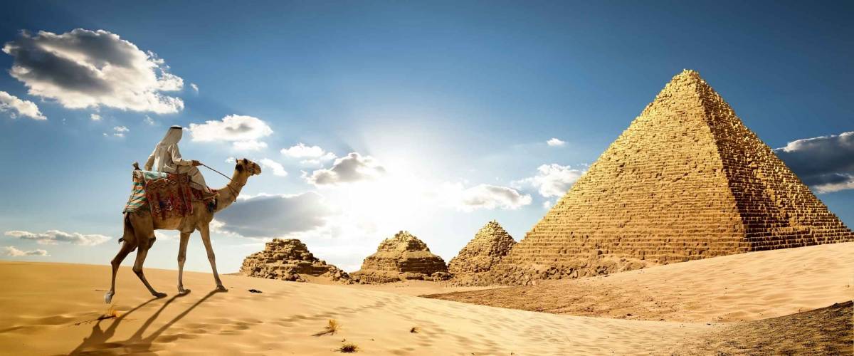Bedouin on camel near pyramids in desert