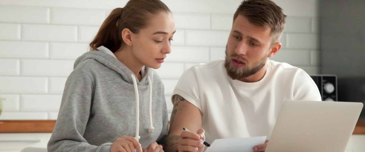 Focused young couple in kitchen discussing whether to refinance their mortgage.