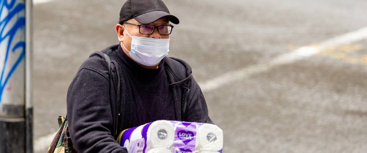 man wearing face mask walks with large case of paper towels
