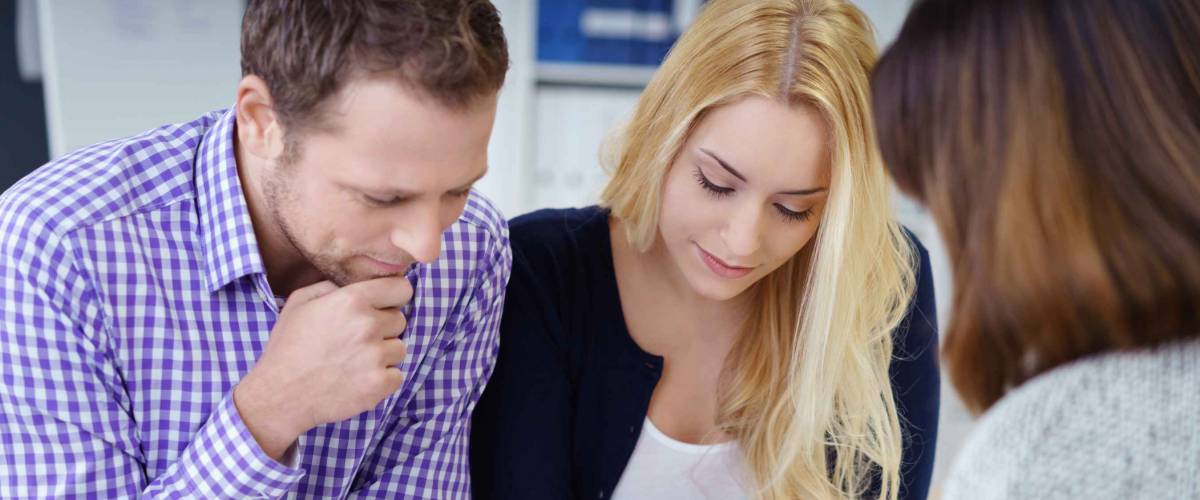 thoughtful looking couple sitting down, facing woman