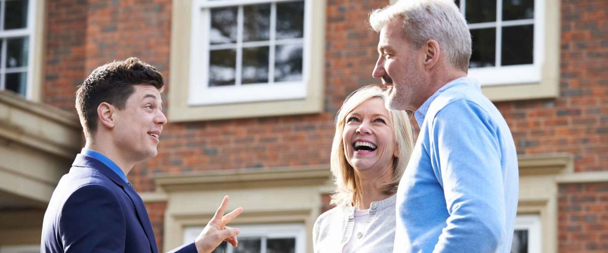 realtor chatting with happy older couple in front of home