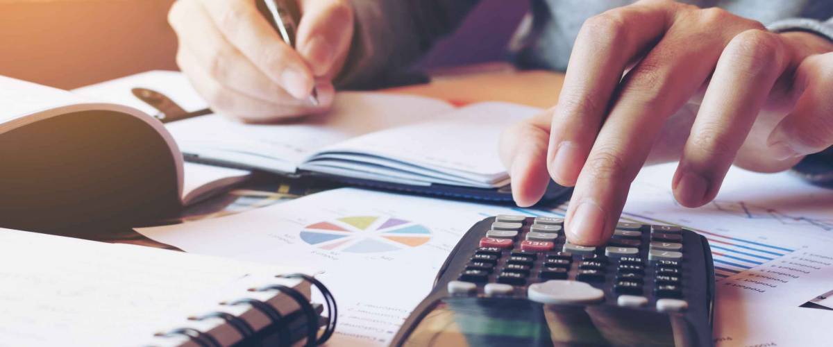 man's hands doing calculations and holding pen