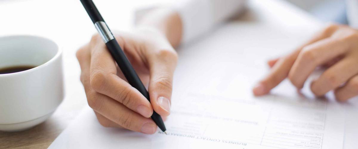 close up of woman's hands holding pen, filling out paper form