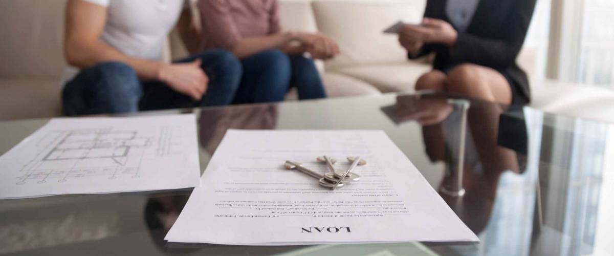 Young family couple sitting on sofa discussing first mortgage with agent, focus on loan agreement and keys,