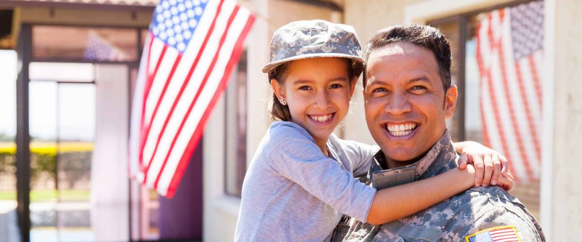 portrait of us army soldier and young daughter outside their home with american flag in background