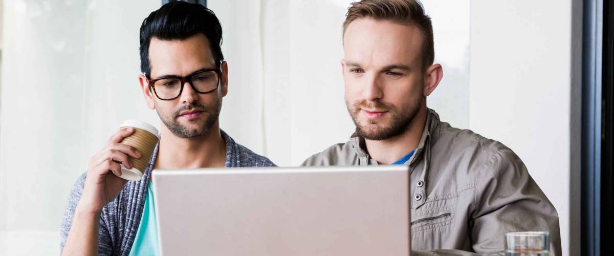 Focused gay couple using laptop outdoors