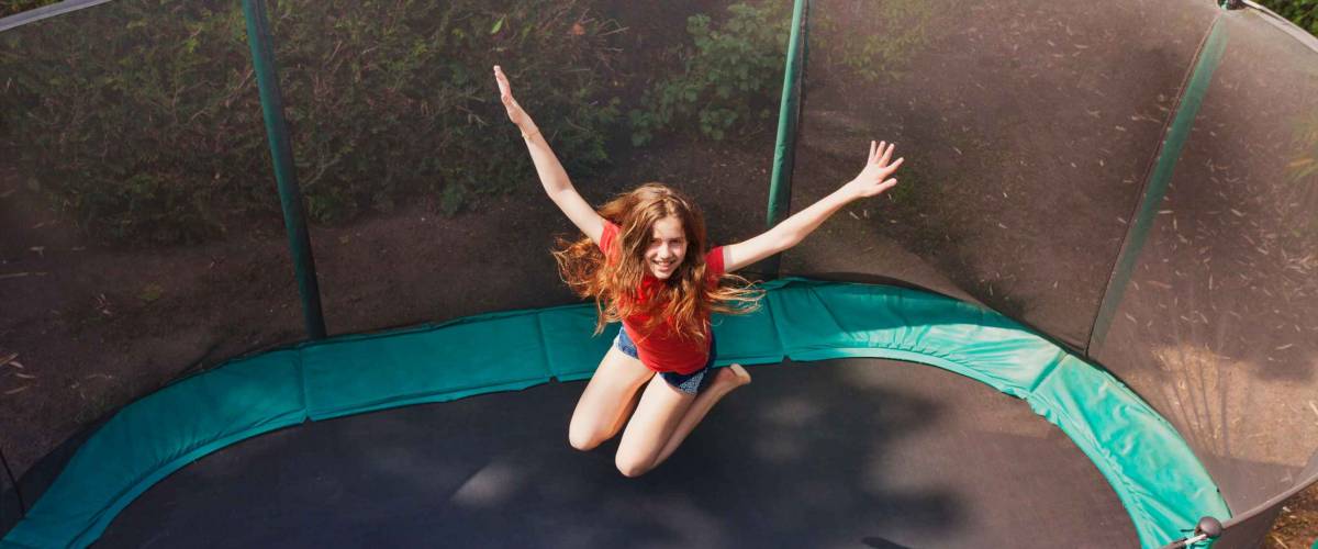 Happy teenage girl jumping on trampoline outdoors