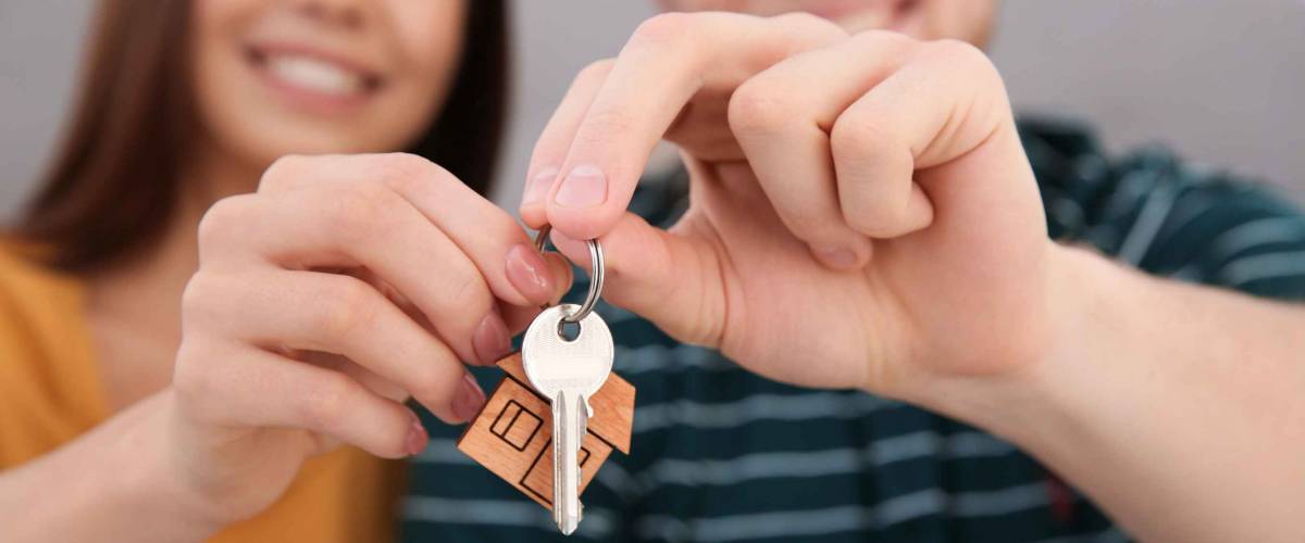 Young couple with key from their new house indoors, closeup. Moving day