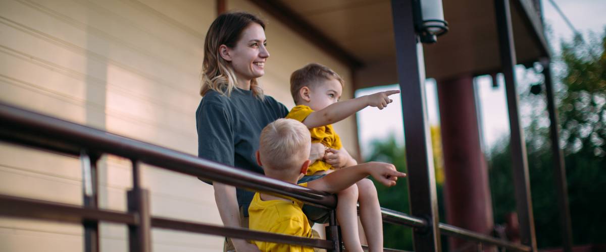 Mom and two sons outside of home, looking into distance