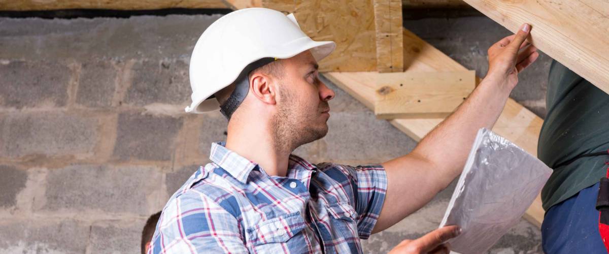 man in construction hat looks at unfinished staircase in basment