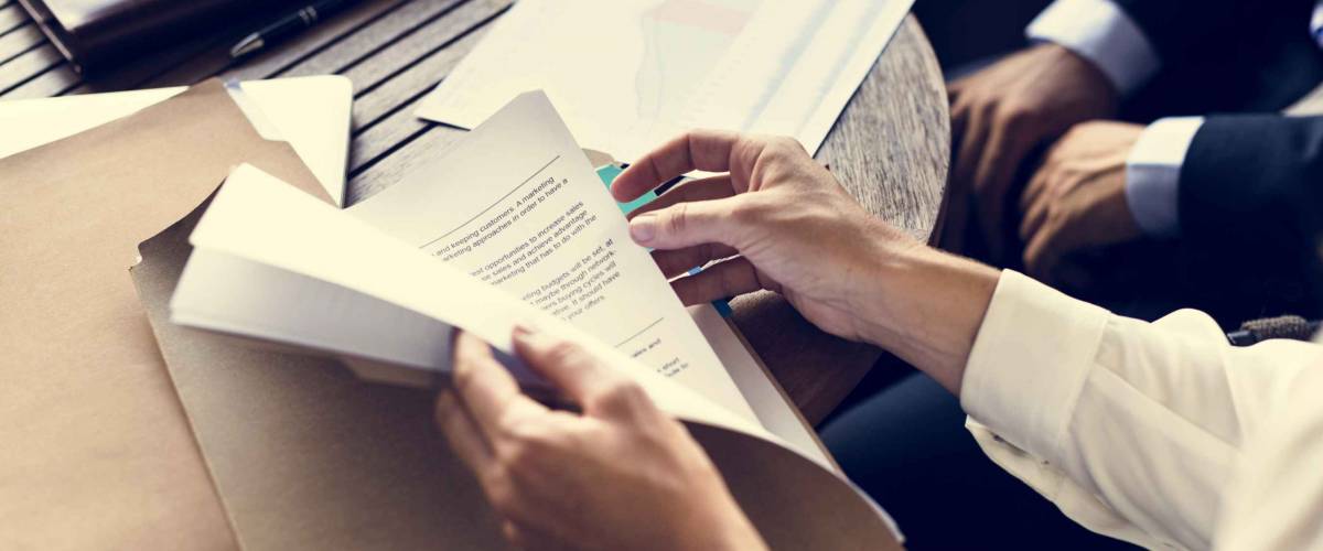 hands opening folder with papers in it on top of wood table